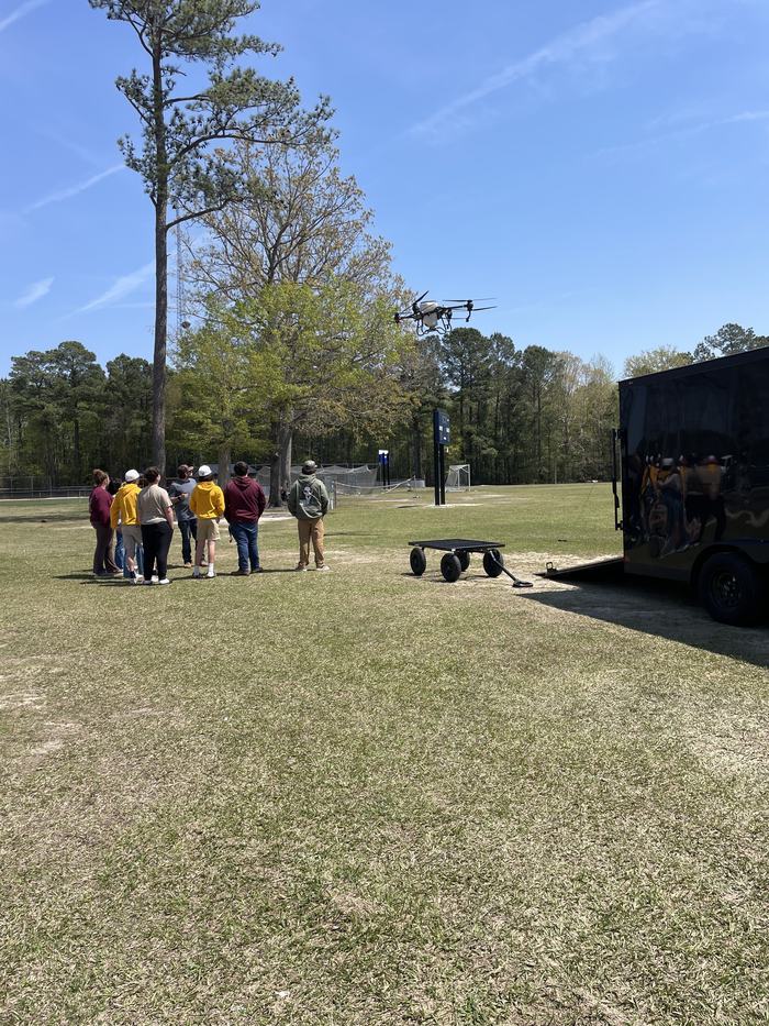 Children stand near a flying drone.