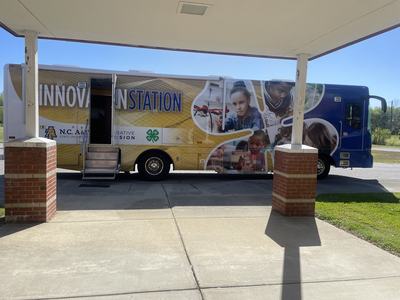 Mobile "INNOVATION STATION" bus parked under a canopy with open side door and step