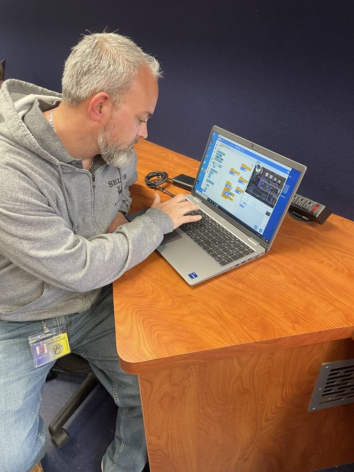 An adult sits at a laptop to help create a game.