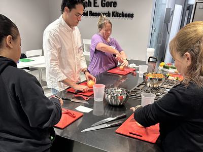 Four people at a counter cutting onions and vegetables in a kitchen labeled "Research Kitchens"