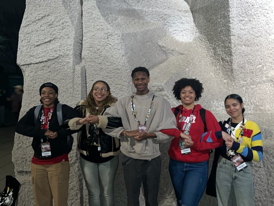 Students link arms in front of a monument.