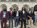 Group of young men in suits and backpacks standing outside a marble building