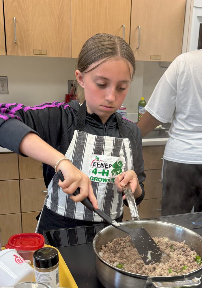 A girl browns meat in a pan.
