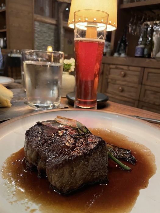 A steak with drinks in the background.