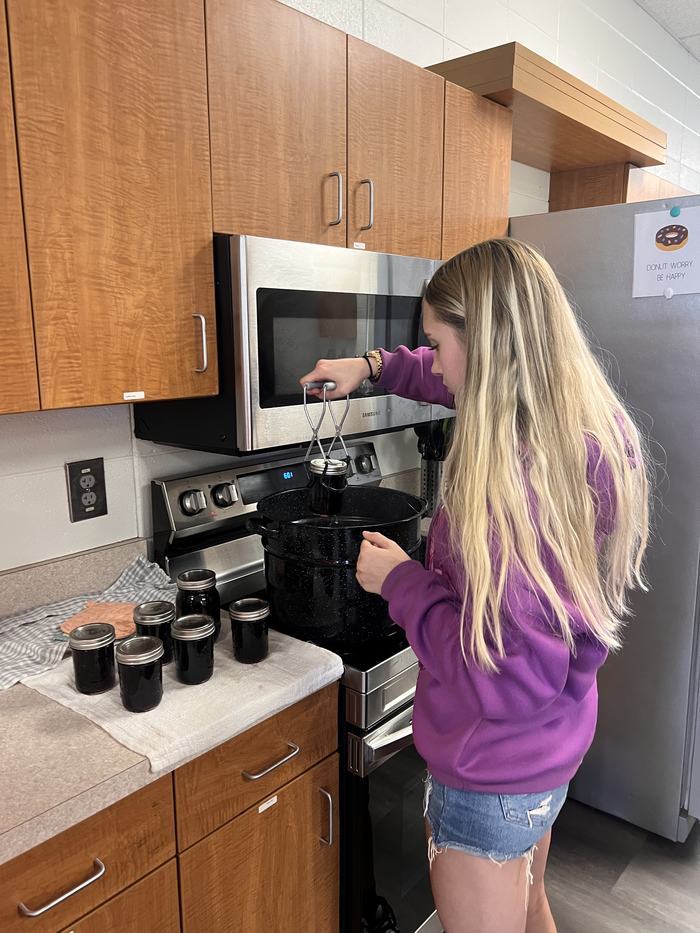 A student places jars of jelly in a canning vessel.