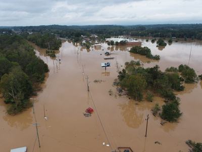 Aerial view of flooded road with submerged buildings, trees, cars, and utility poles