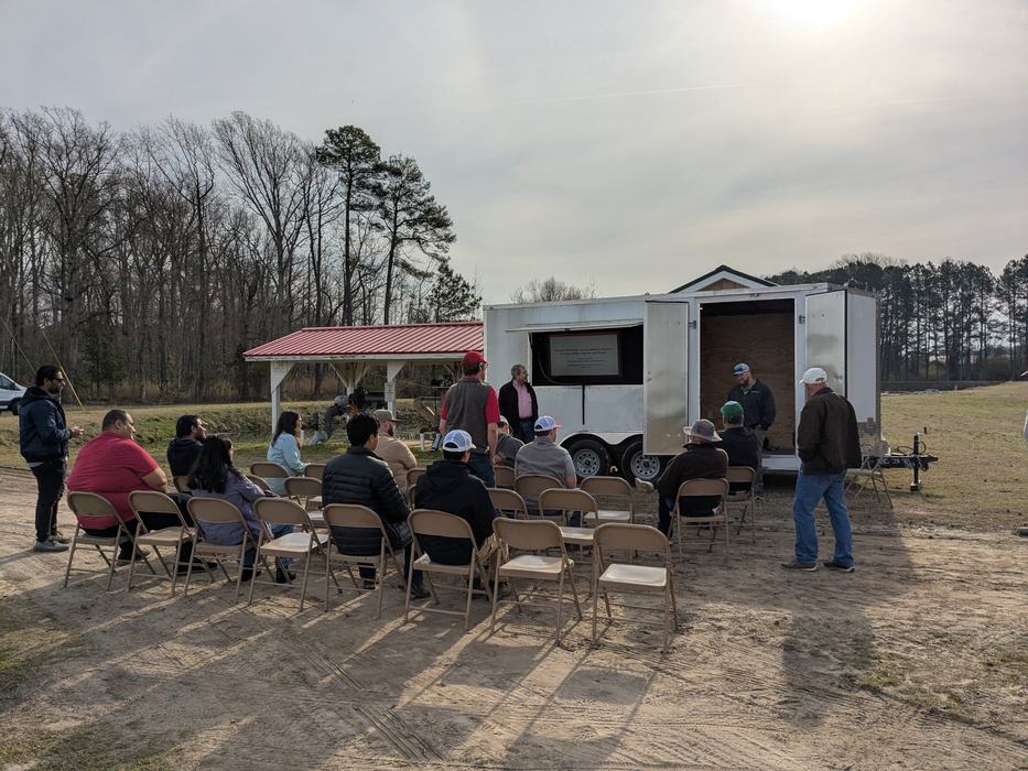 Group of people seated outdoors watching a presentation displayed from an open trailer