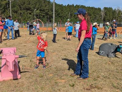 Child practicing lassoing a dummy steer while adults watch in a rodeo arena