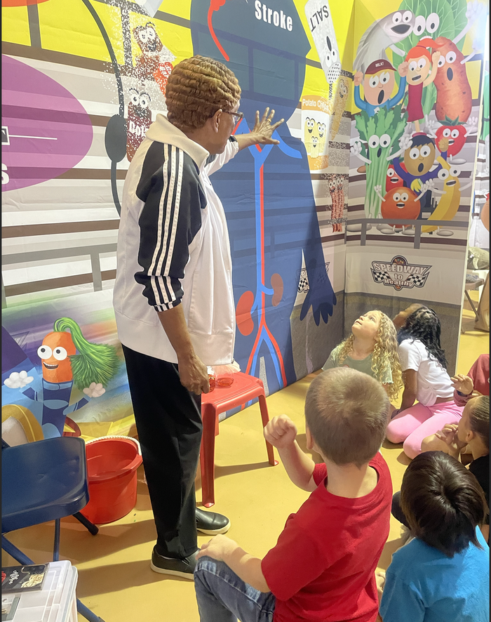 Adult pointing at anatomy poster labeled Stroke while children sit and watch