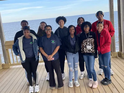 Eleven teens standing together on a wooden pier by the water.