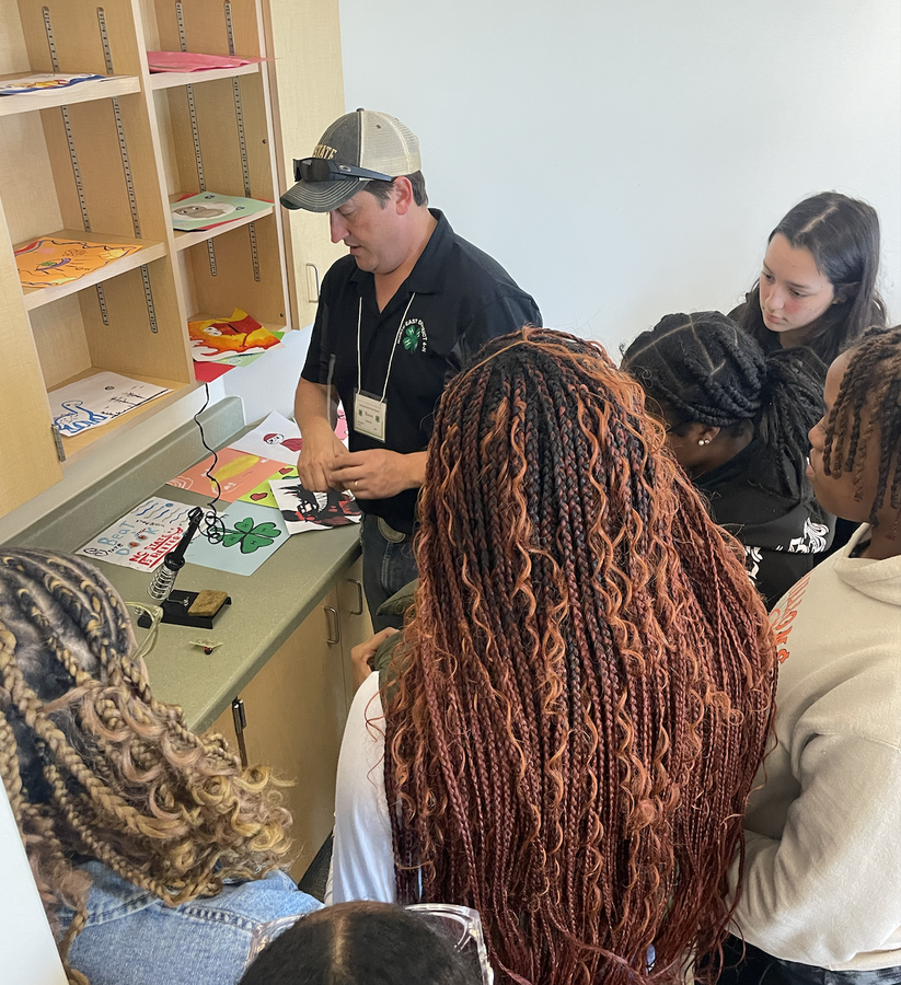 A man shows students how to use a wood burning tool.