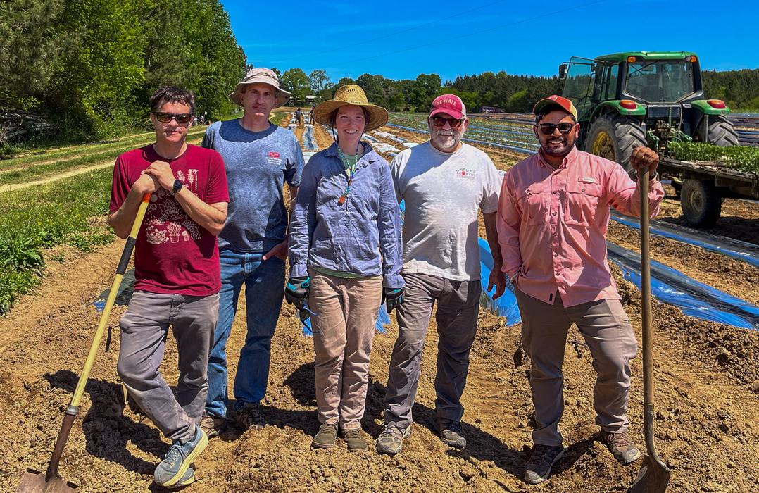 Walgenbach Lab members doing field work on a farm with tractor in background