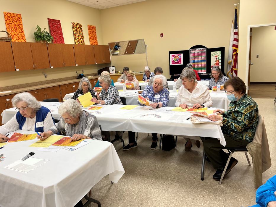 Older adults seated at tables reviewing papers and pamphlets in a classroom setting