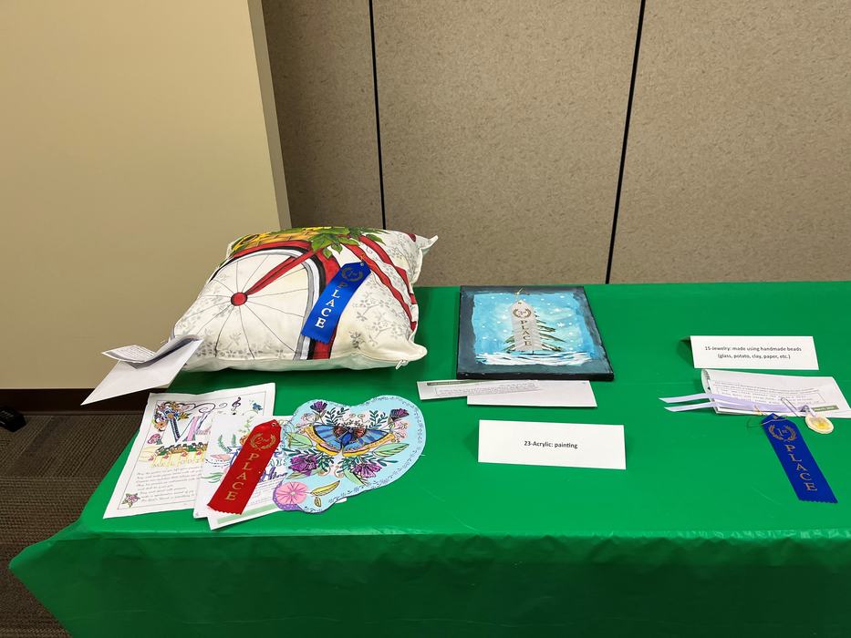Table display of art entries: decorated pillow, acrylic painting, heart drawing with ribbons