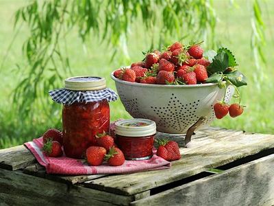 colander of fresh strawberries and jars of jam on a crate.