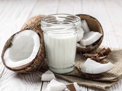 Mason jar of milk or yogurt on hemp napkin on white wooden table with coconut aside