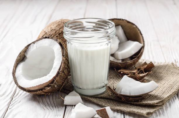Mason jar of milk or yogurt on hemp napkin on white wooden table with coconut aside