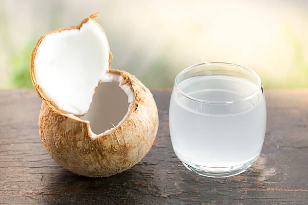 Glass of fresh coconut juice and opened coconut fruit on palm leaf, vintage wooden background with copy space.