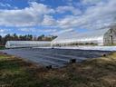 Two plastic-covered hoop greenhouses beside tarped ground under partly cloudy sky