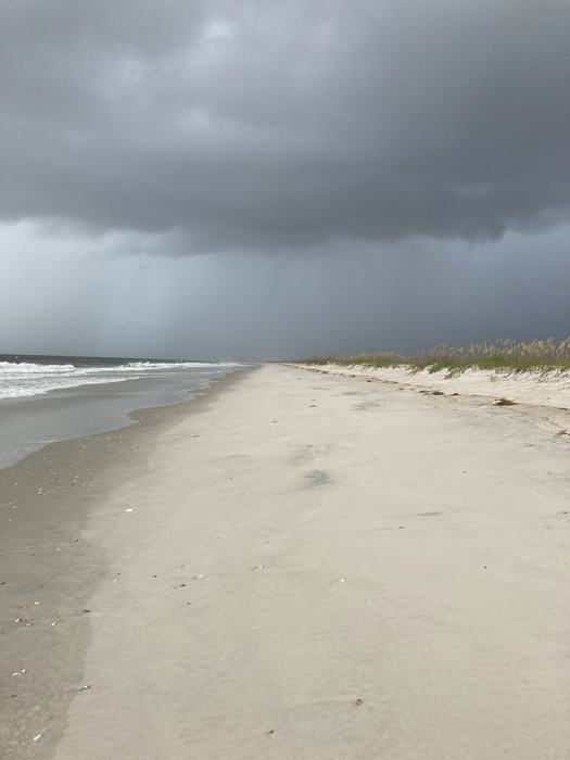Sandy beach shoreline with waves and dark storm clouds approaching