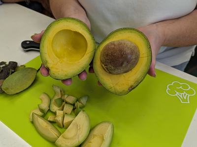 Person holding two avocado halves over green cutting board with sliced avocado pieces.