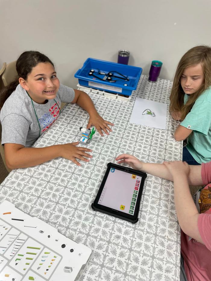 Three kids at table using a tablet to program small LEGO-style robotics pieces
