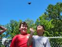 Two boys by a chain-link fence looking up as a butterfly flies overhead