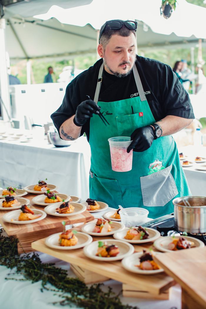 Man in turquoise apron labeled "CHEF JASON" plating appetizers with tweezers