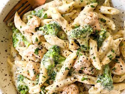 Bowl of creamy penne pasta with broccoli and small meatballs, fork at bowl edge
