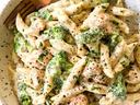 Bowl of creamy penne pasta with broccoli and small meatballs, fork at bowl edge