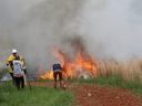 Three people near a grass fire, one bending to use a fire extinguisher