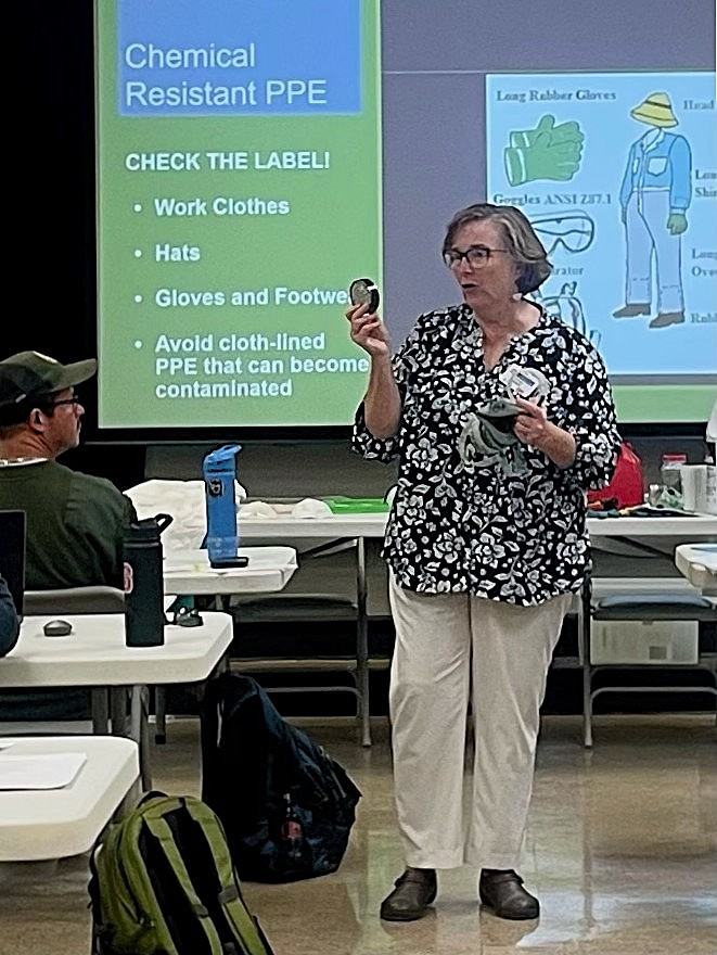 A woman teaching a class about chemical-resistant PPE while holding a respirator mask and cartridge filter