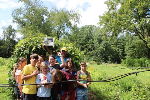 Children and an adult under a leafy garden arch, one person holding a paper
