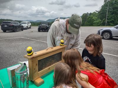 Beekeeper showing a hive frame with bees to three children leaning in