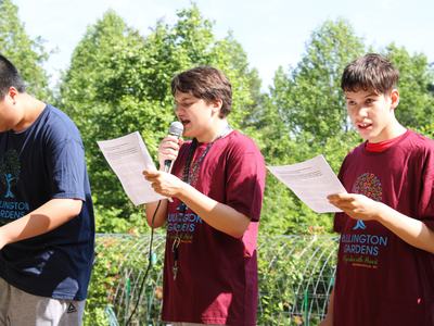 Students read into a microphone in a garden.