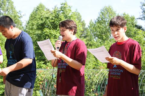 Students read into a microphone in a garden.