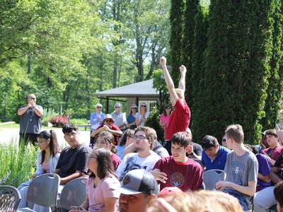 Young person standing with arms raised among seated crowd outdoors