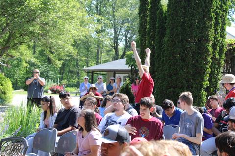 Young person standing with arms raised among seated crowd outdoors
