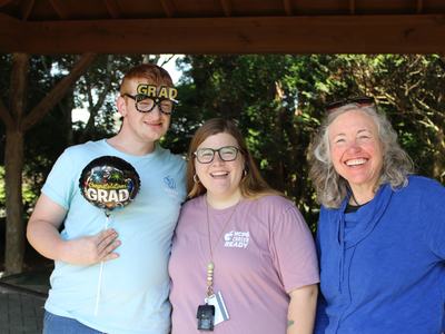 A graduate poses with two others under a shelter.