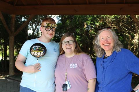 A graduate poses with two others under a shelter.