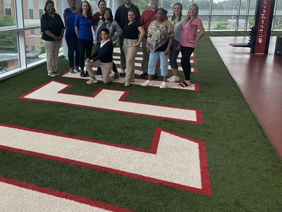 Group of people posing on indoor turf field with large white-red letters
