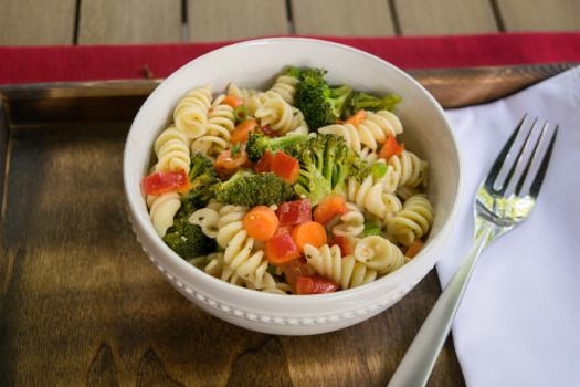 Rotini pasta in a bowl with broccoli, carrots and peppers.