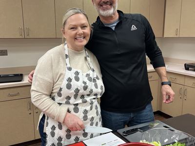 two people standing in front of a cutting board with vegetables