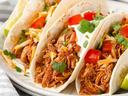 Three shredded chicken tacos with cheese, diced tomato, cilantro, and sour cream
