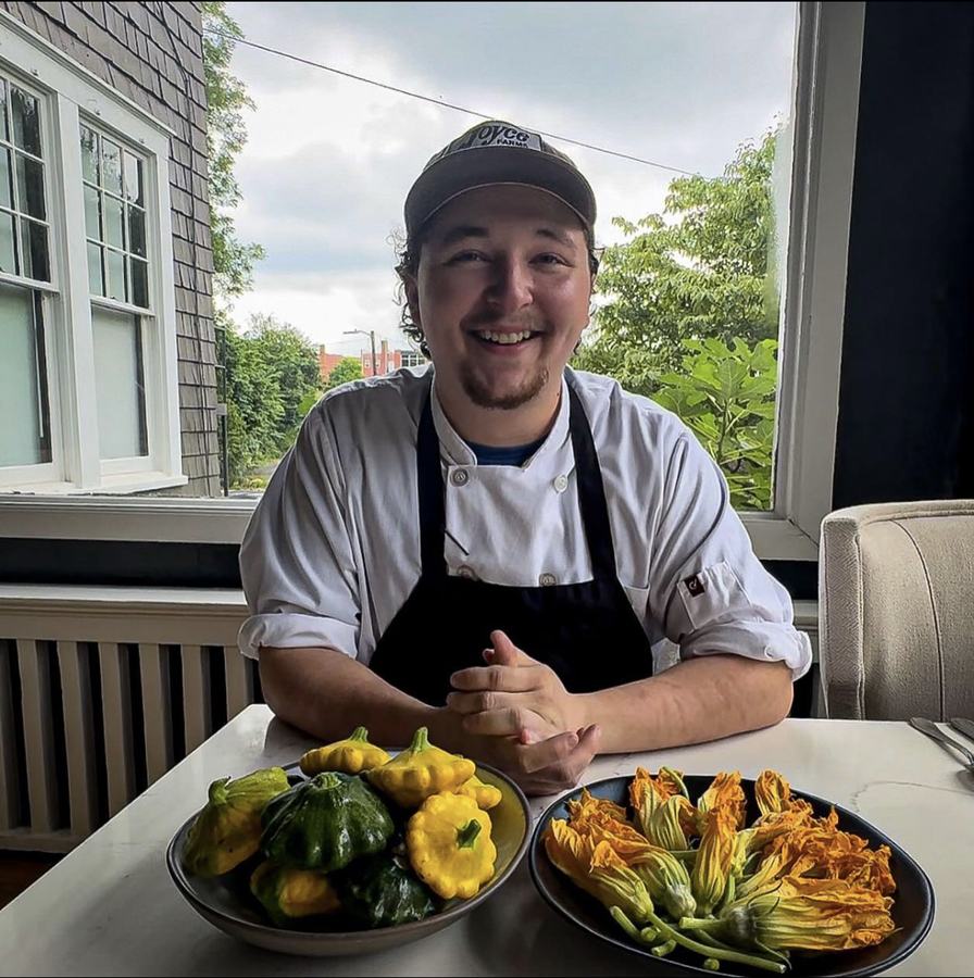 Chef in uniform at table with bowls of pattypan squash and squash blossoms