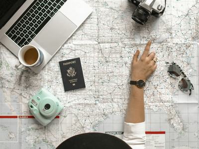 map with passport, camera, sunglasses, and laptop on top