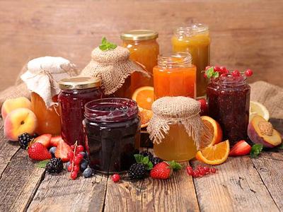 Jars of assorted fruit jams and marmalades with fresh berries and sliced citrus on wood