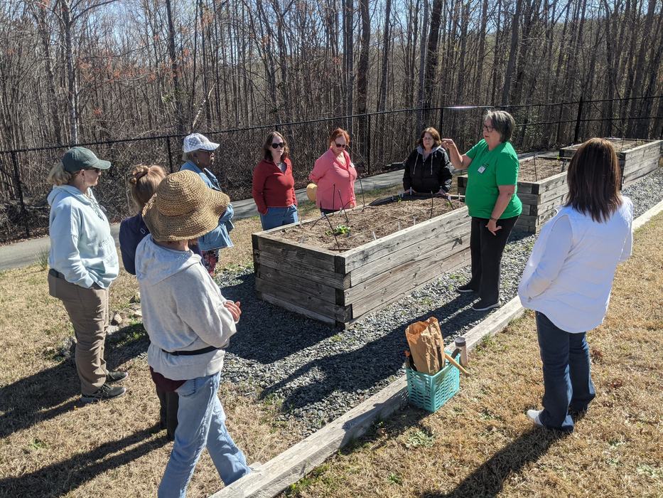 Group of people gathered around raised garden beds while one woman gestures and speaks