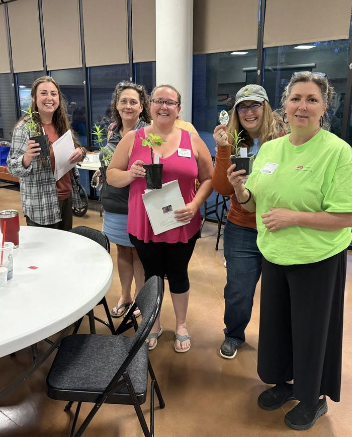 Five people standing indoors holding small potted plants and papers