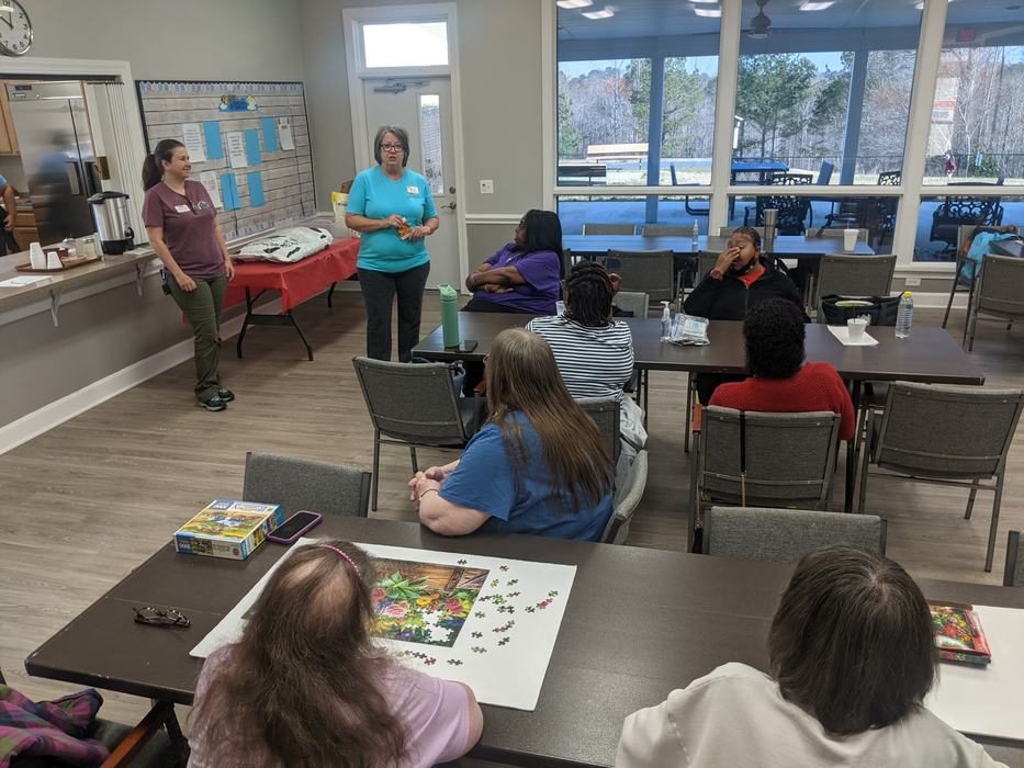 People seated at tables listening to two women speaking in a community room